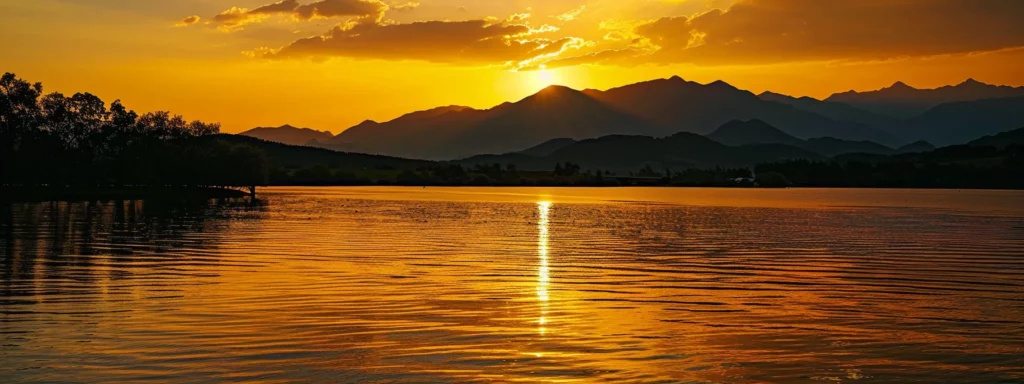 a vibrant sunset casts golden hues over a tranquil lake, with silhouetted mountains framing the horizon, creating a serene and picturesque landscape.