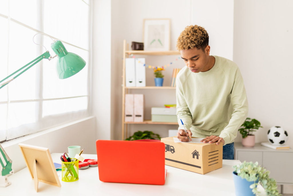 Hispanic latin young seller man preparing second hand package before sending to buyer - Young male seller writing address on box
